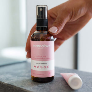 Hand holding Mamalove Body Oil on a bathroom counter, emphasizing its role in the daily skincare routine of pregnant women